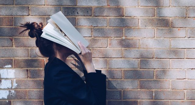 Eine Studentin hält ein Buch vor ihren Kopf